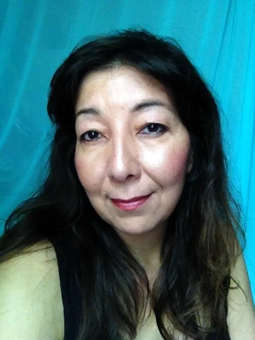 Tracey Nepinak looks directly at the camera with a gentle smile and long, dark hair. She is captured in a headshot against a vibrant, draped turquoise background.